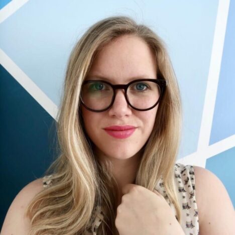 A blonde woman with glasses looking at the camera