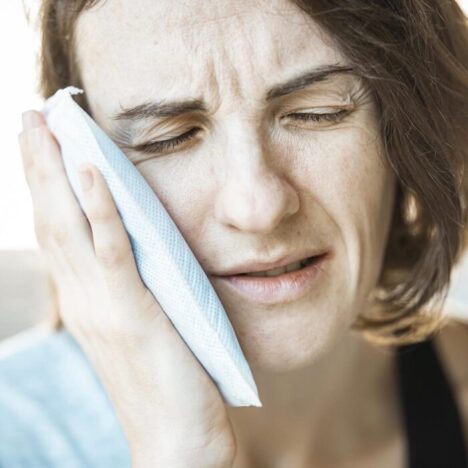 A woman holding an ice pack to the side of her face and looking in pain