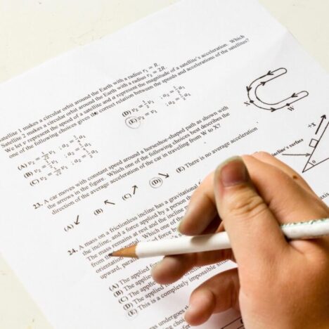 A hand holding a pencil over a physics question paper