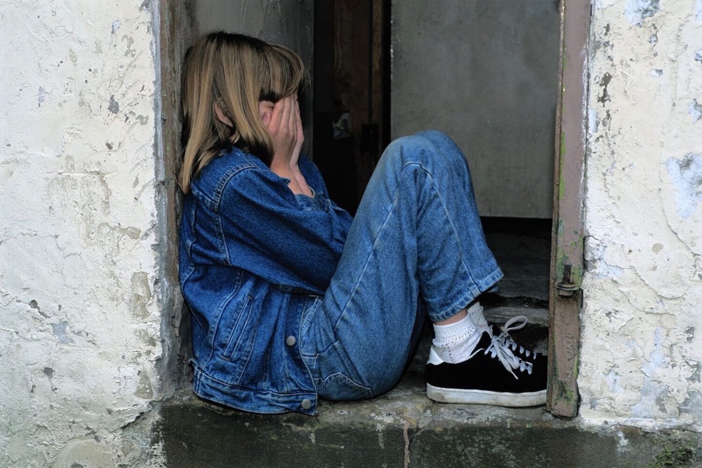 A child sat in a doorway with the hands covering their face