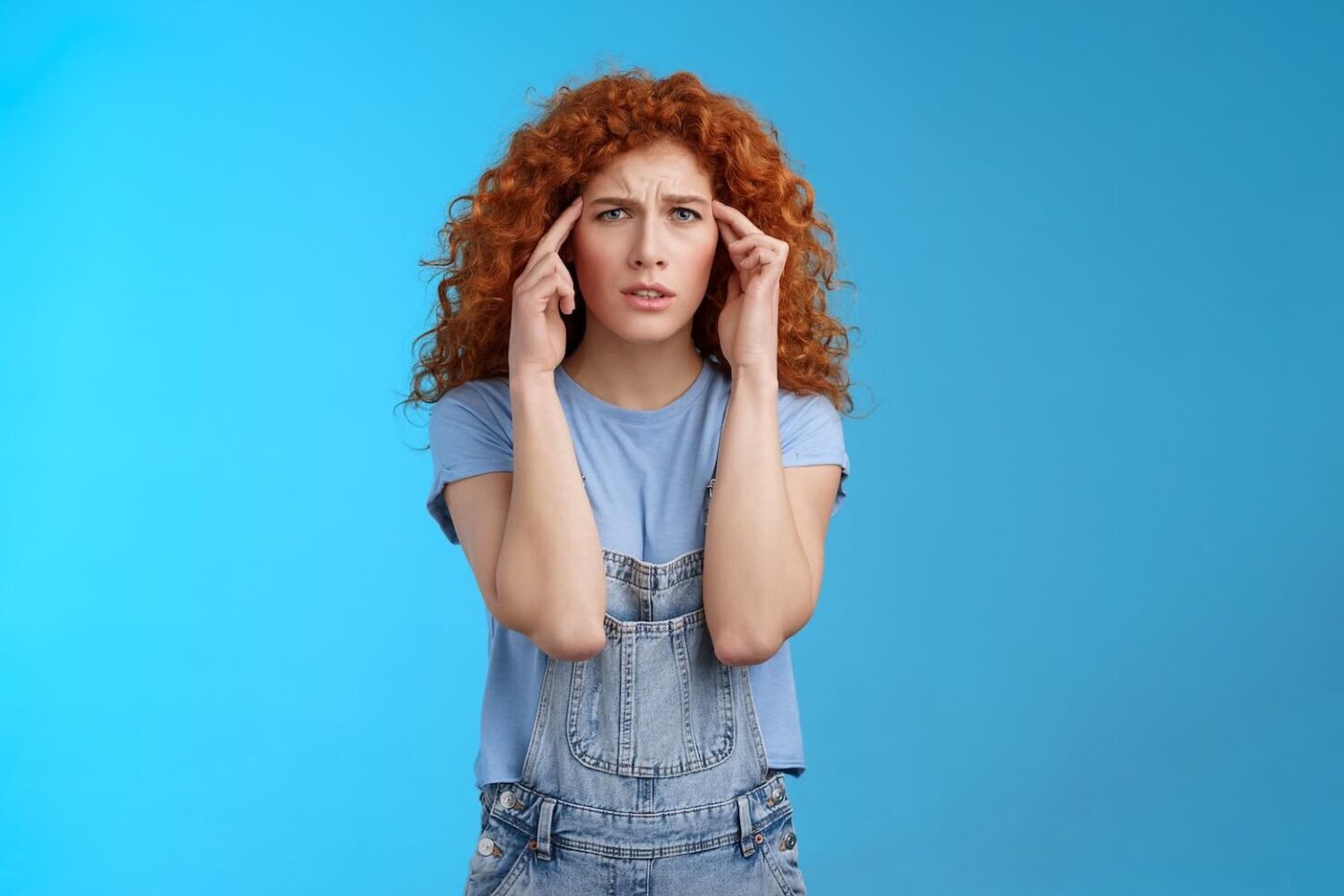 A girl with red curly hair pressing her fingers into the sides of her head
