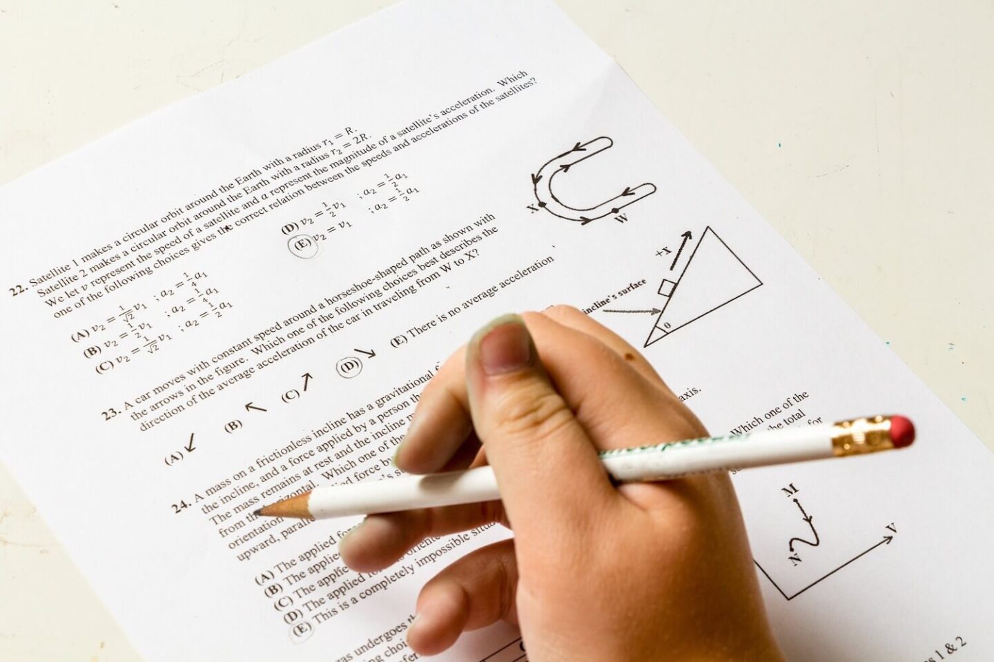 A hand holding a pencil over a physics question paper
