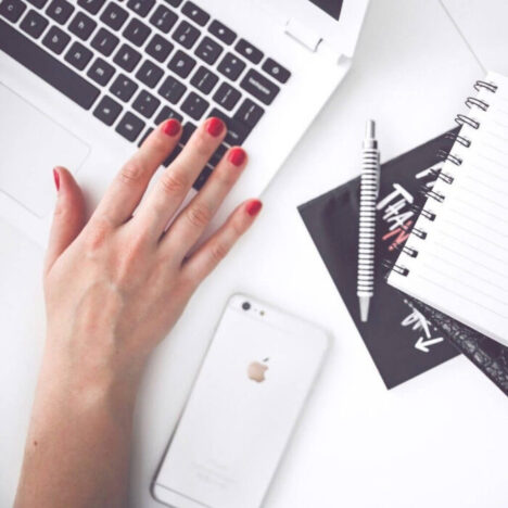 A hand resting on a mac keyboard next to an iphone