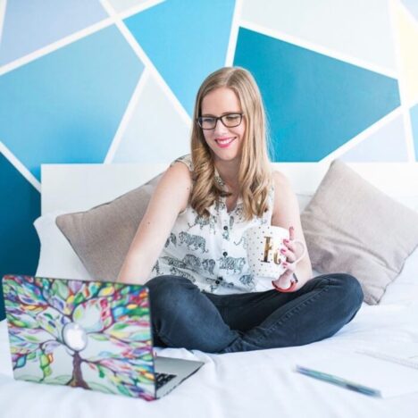 A woman sitting crossed leg on the bed holding a mug and looking at her laptop