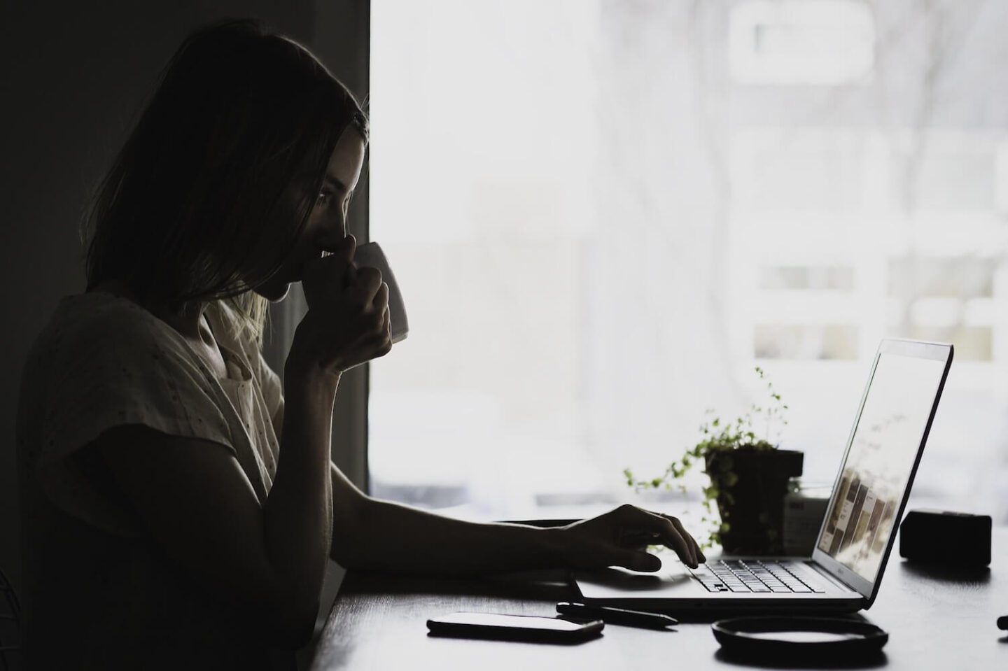 A woman drinking from a mug and looking at a laptop