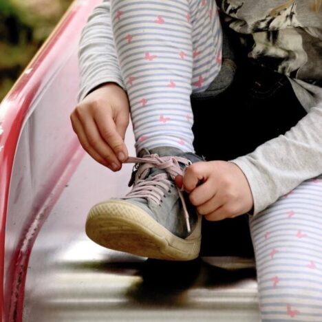 A child sitting on the end of a slide tying a shoelace