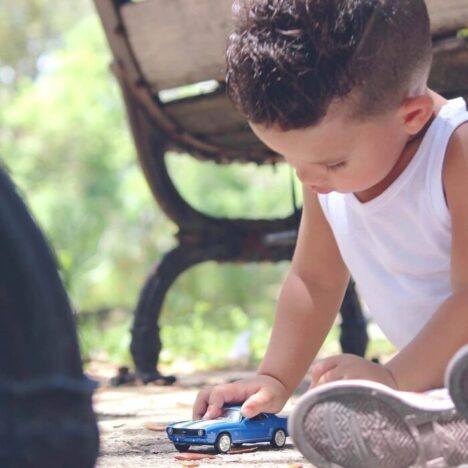 A toddler sitting on the floor pushing a blue toy car around