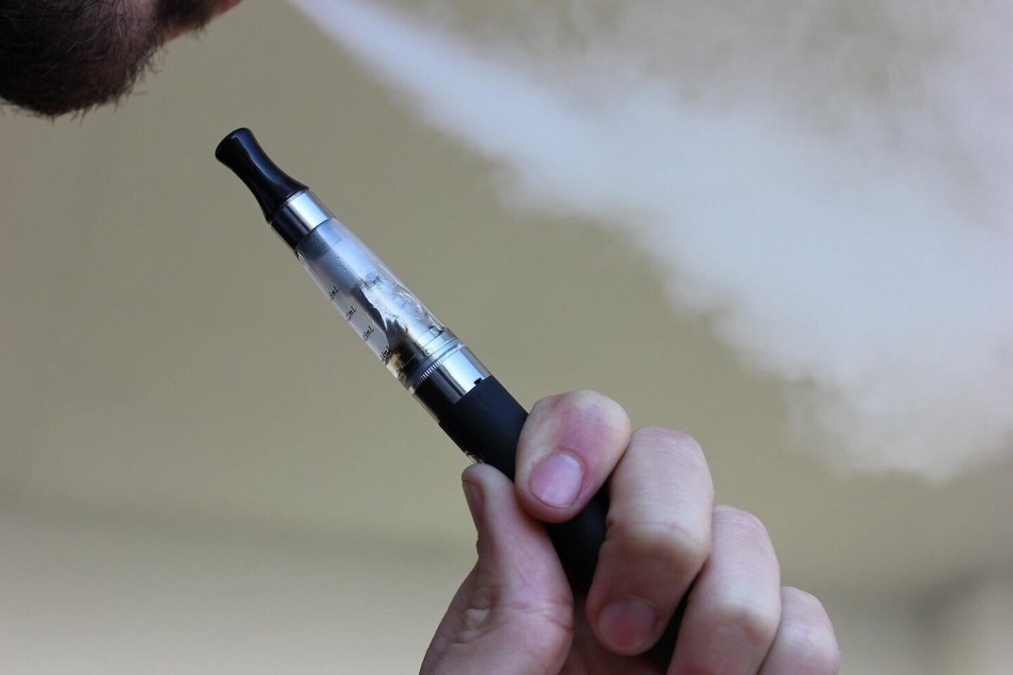 A vape pen being held and a stream of vape being blown out of somebody's mouth