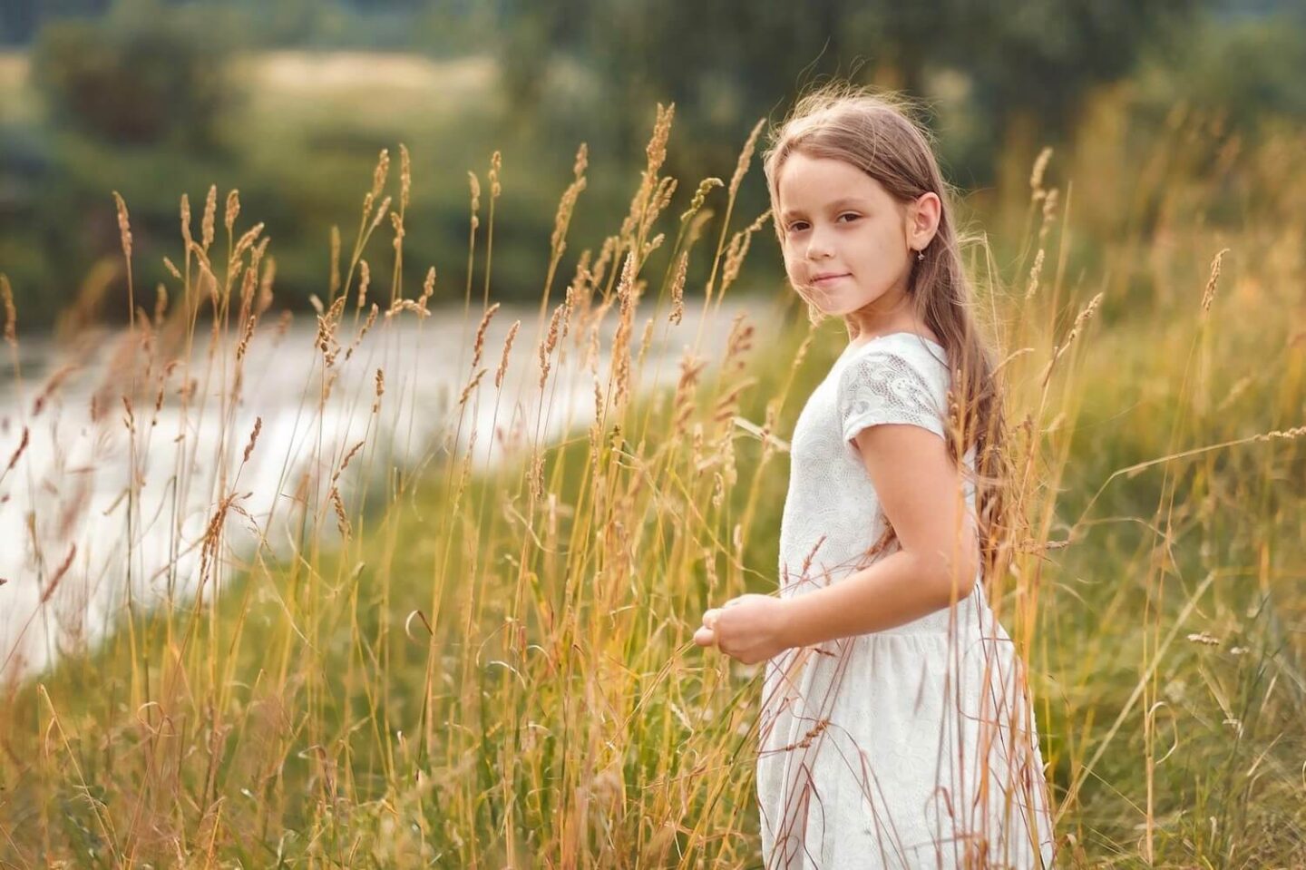 A girl standing in a field of long grass, looking to the side towards the camera