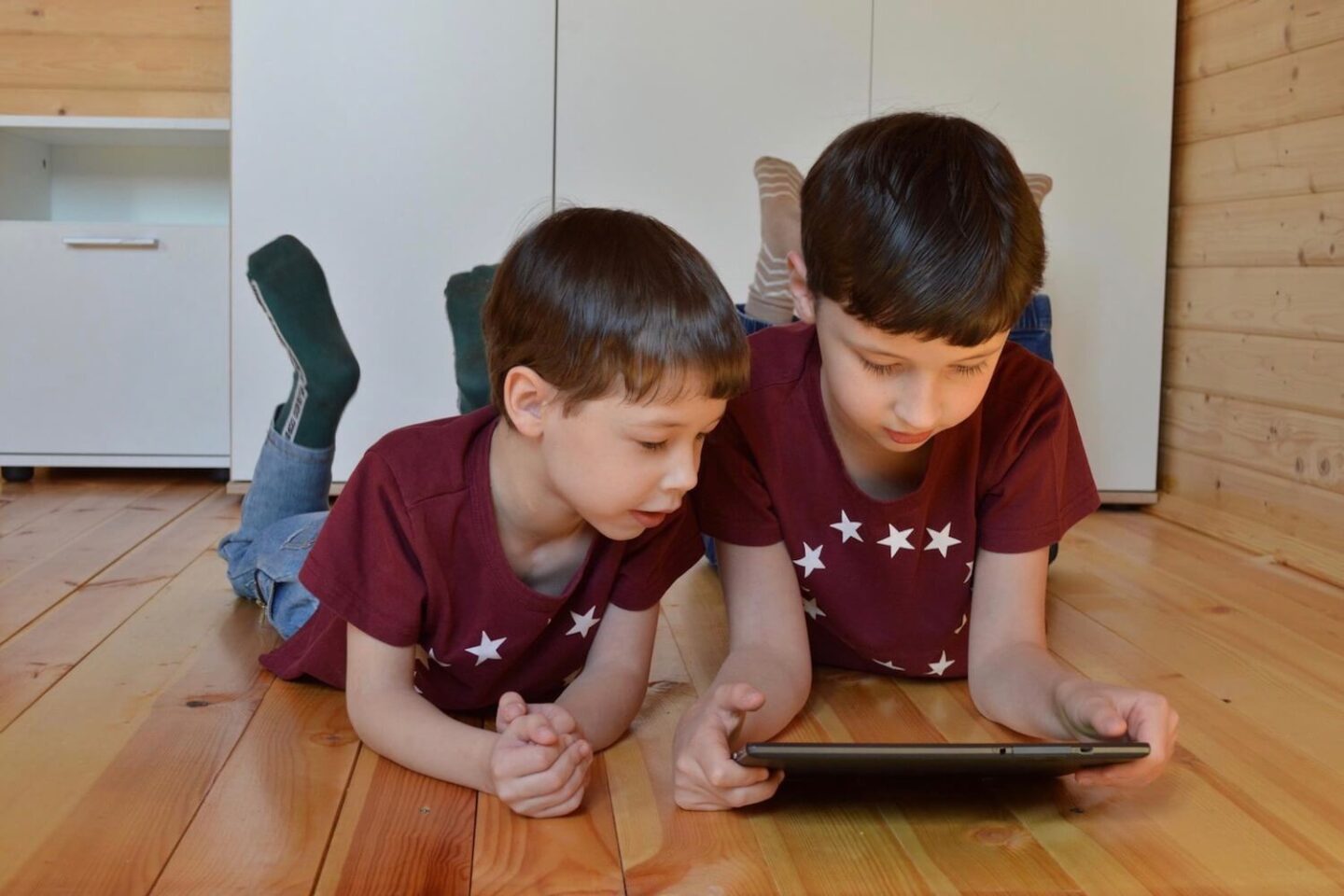 2 boys lying on their stomach looking at a tablet
