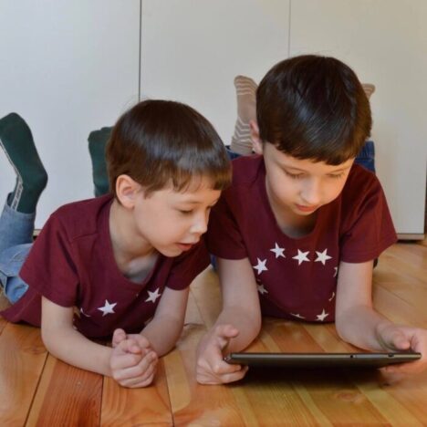 2 boys lying on their stomach looking at a tablet