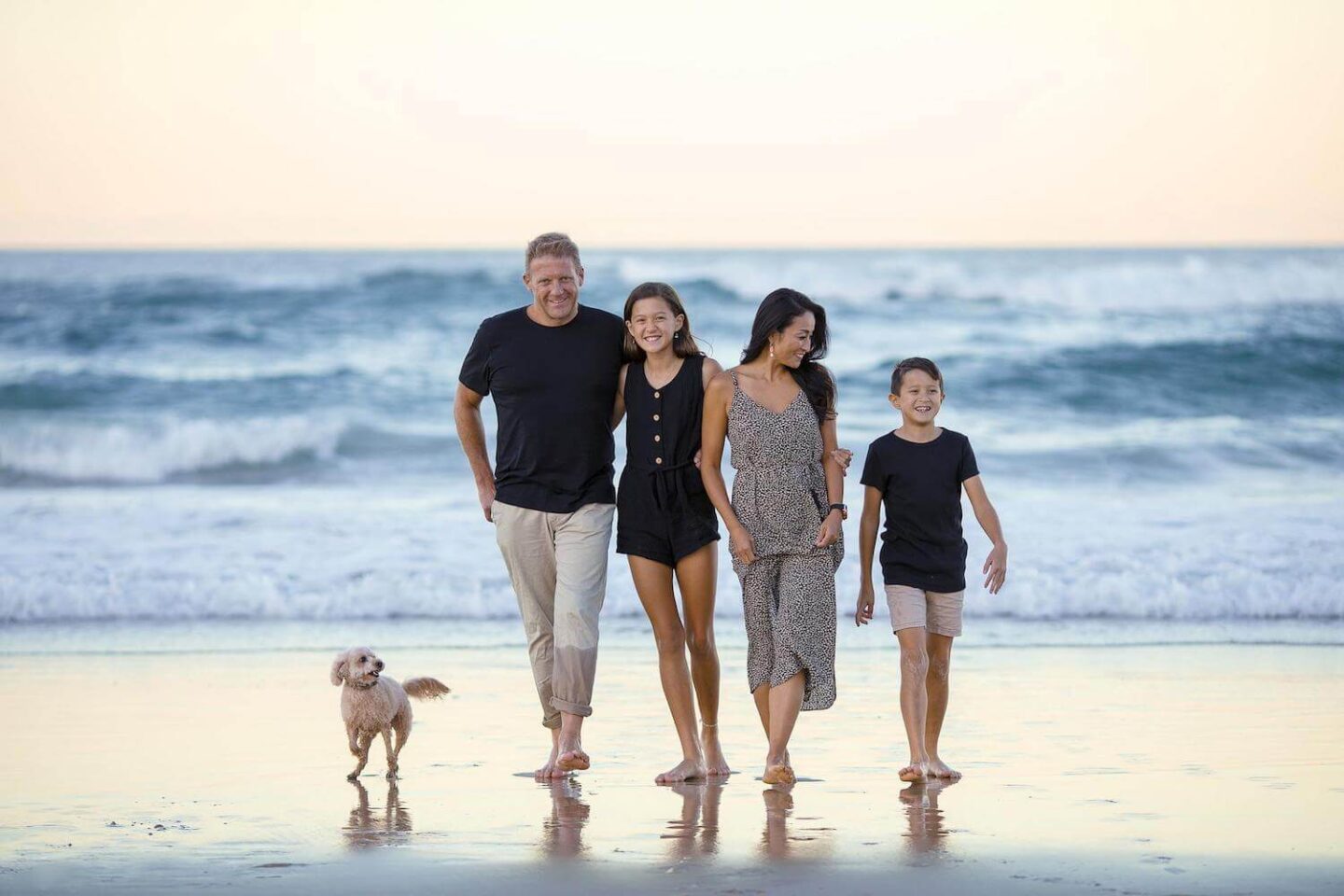 There is a family of mum, dad, daughter and son and a dog walking on the beach away from the ocean