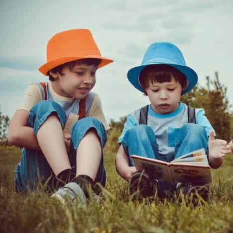 2 boys sitting on the grass looking at a book