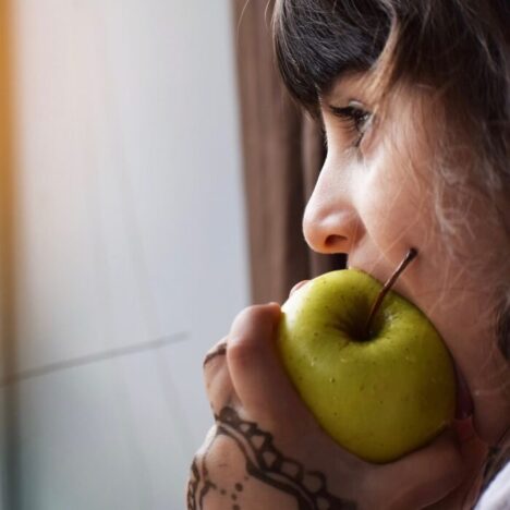 A girl with brown hair taking a bite out of a green apple