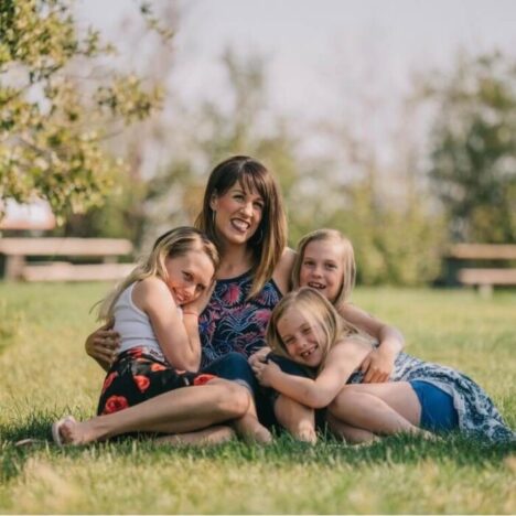 A woman and 3 girls hugging on the grass
