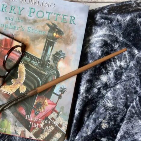 A Harry Potter book, magic wand and glasses lying on an invisibility cloak