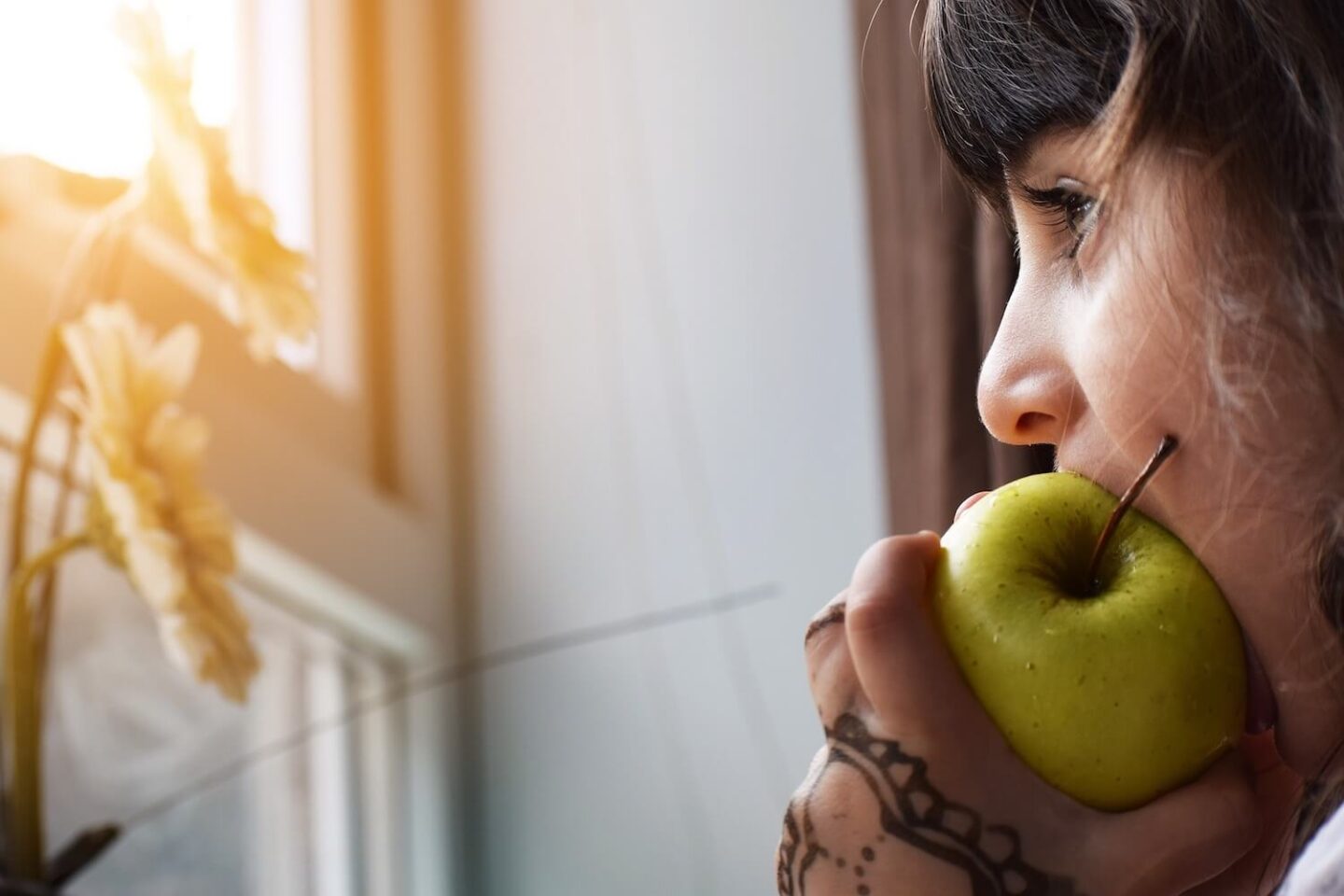 A girl with brown hair taking a bite out of a green apple