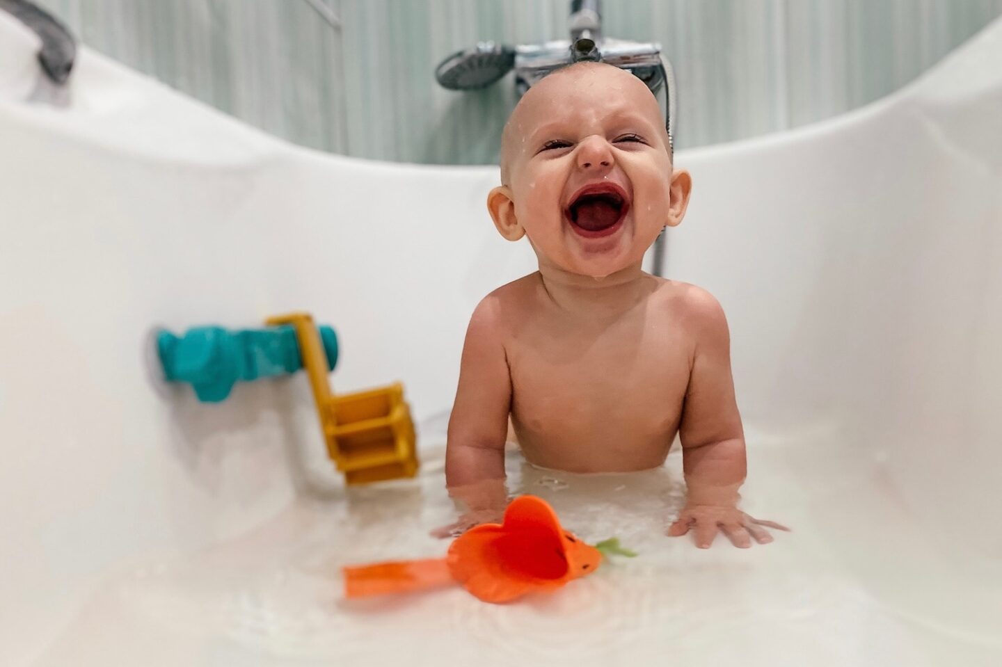 A baby in a shallow bath laughing and smiling
