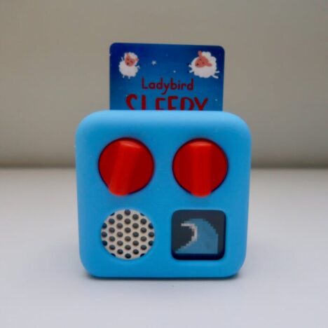 A Yoto mini wearing a blue adventure jacket. The mini screen is showing a large wave