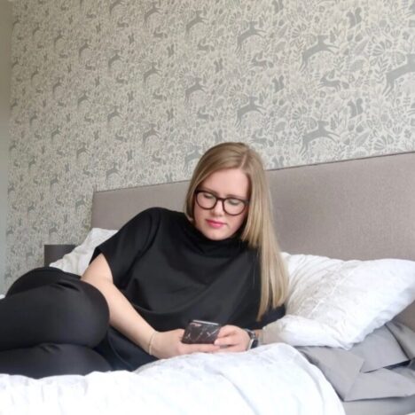 A woman lying on her side on a bed and looking at her phone