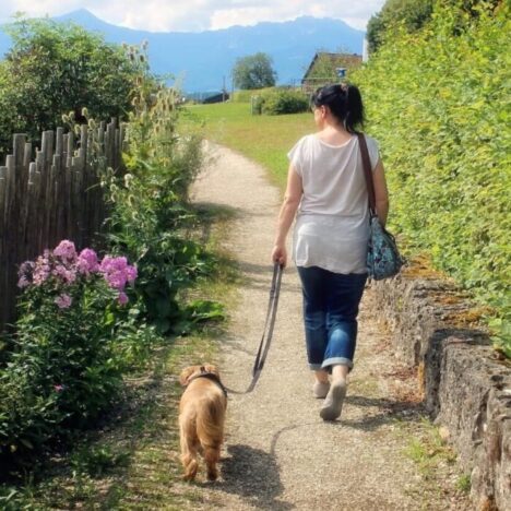 A woman walking down a lane in the countryside with a dog on a lead.
