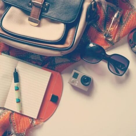 A bag, open notebook, go-pro camera all laid on the floor
