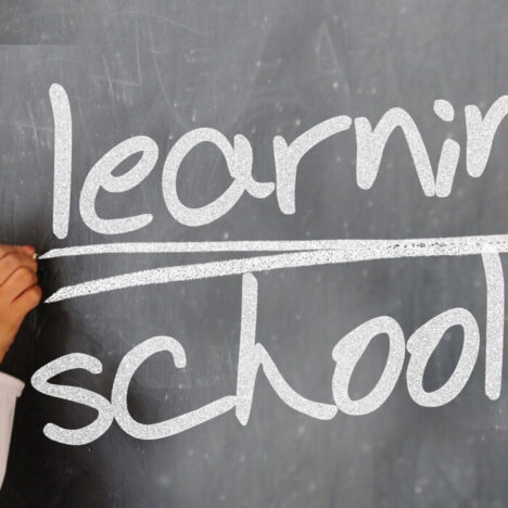 White chalk writing on a blackboard reading "learning schooling"