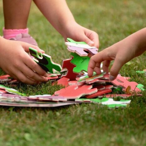 The hands of 2 children sorting jigsaw pieces on some grass