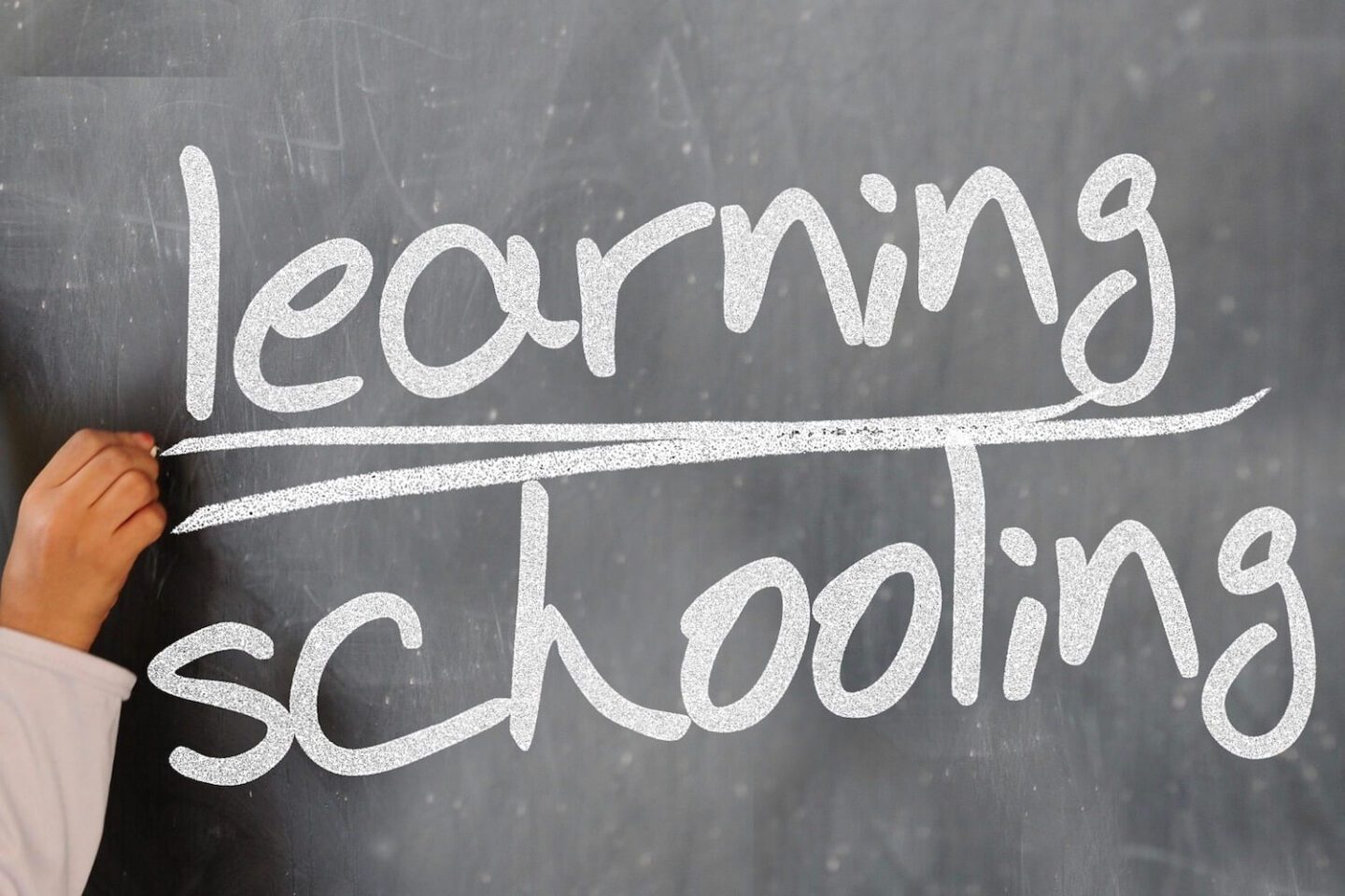 White chalk writing on a blackboard reading "learning schooling"