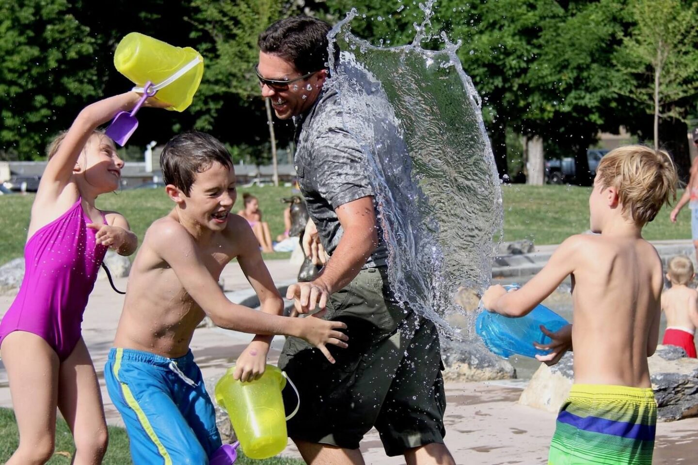 A family having a water fight. Children are throwing buckets of water over a man