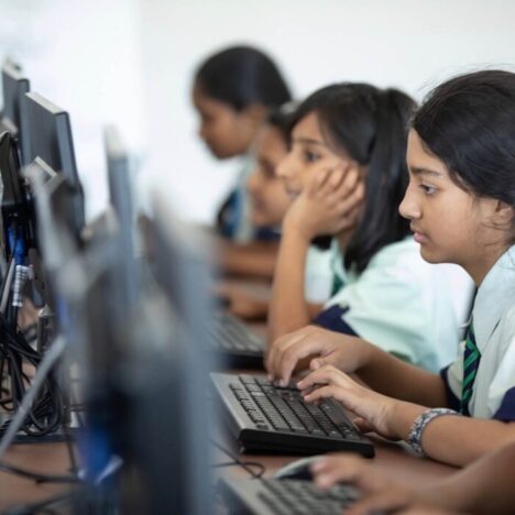 Children in school uniforms sitting at a row of computers working.