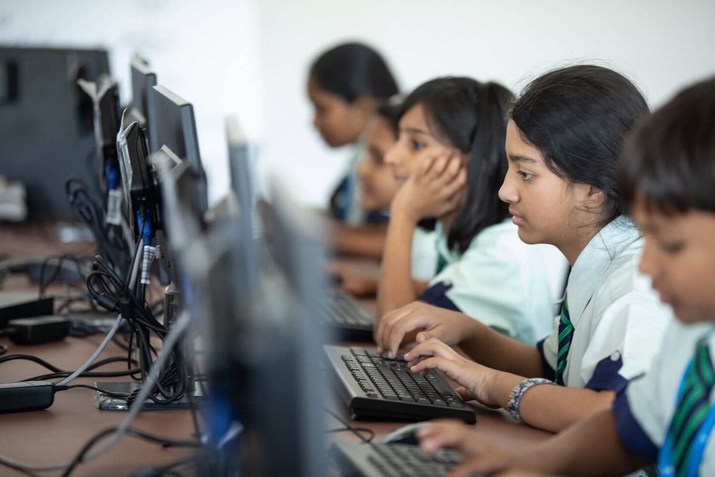 Children in school uniforms sitting at a row of computers working.