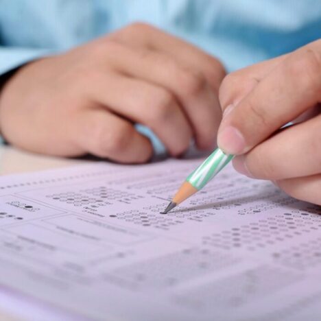 A hand holding a pencil and writing on an exam paper