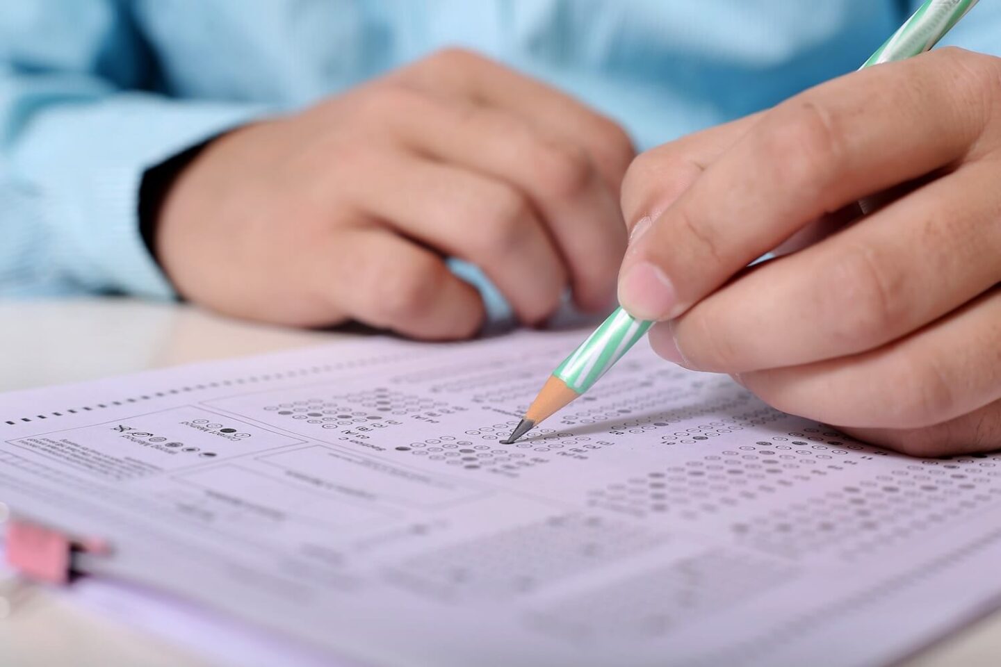 A hand holding a pencil and writing on an exam paper