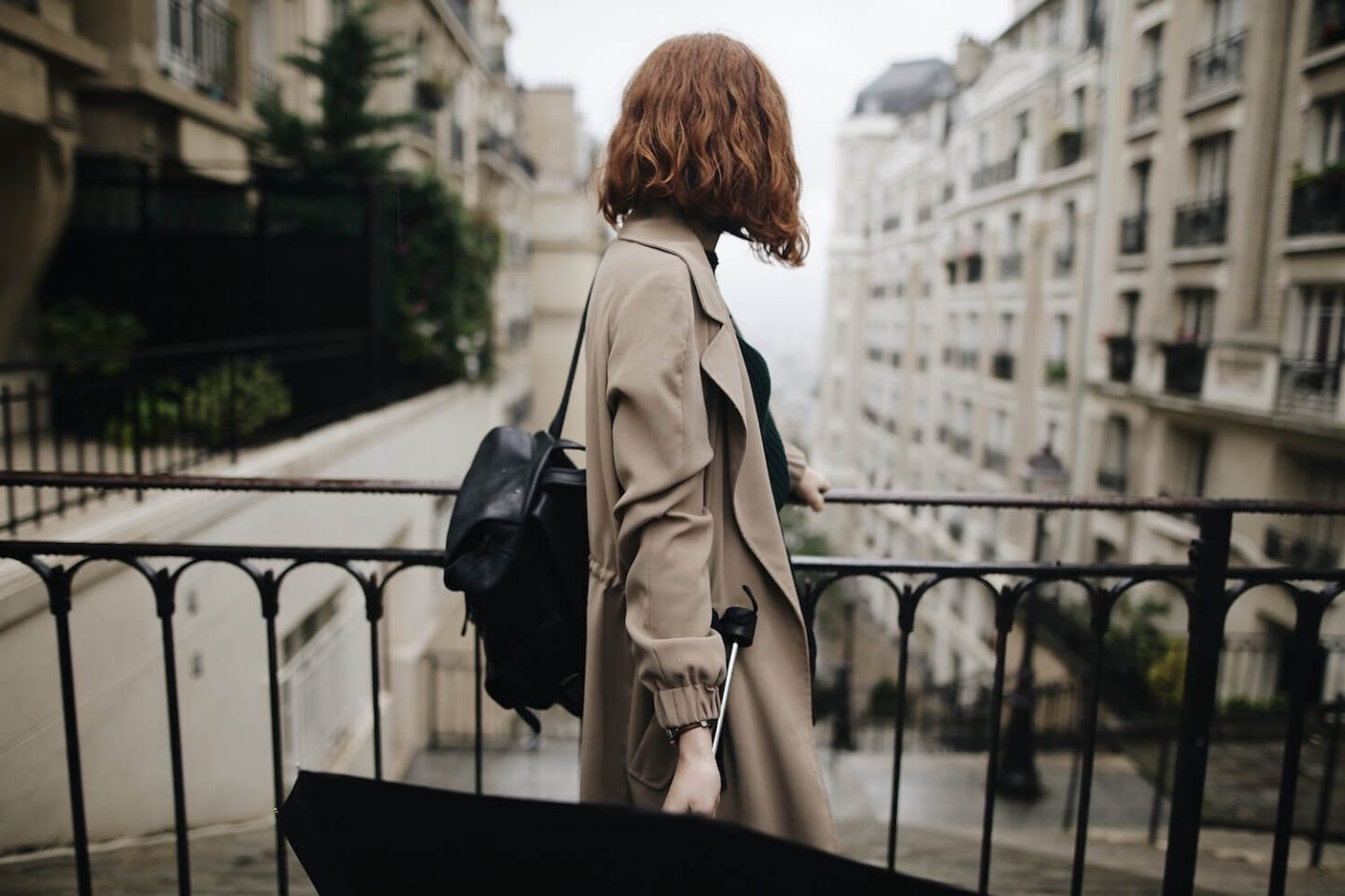 A woman looking over the city, holding a black umbrella by her side