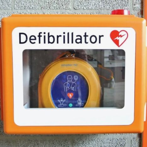 An orange box with a glass front fixed to a wall. Inside is a defibrillator