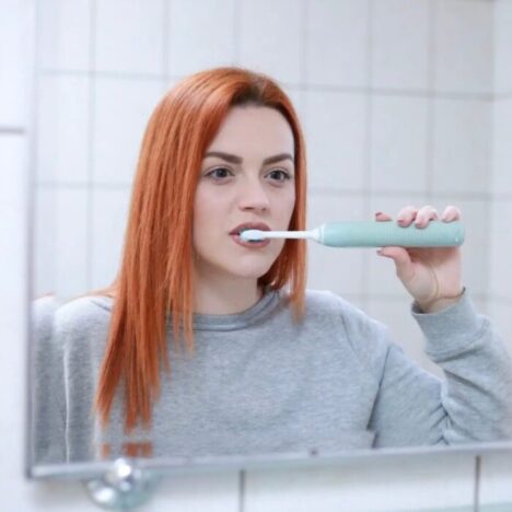 A woman with ginger hair brushing her teeth in the mirror
