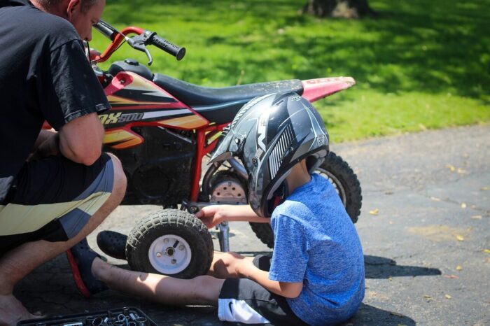 A child sits on the ground next to a miniature motorbike