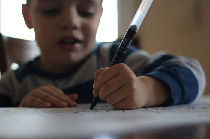 A young boy sitting at a table and writing with a black pen