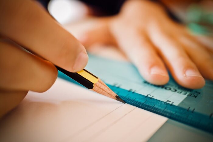 A ruler on a piece of paper with a hand holding a pencil