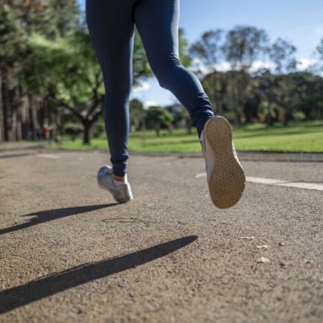 The legs of a person running on the road next to a grassy area on a sunny day