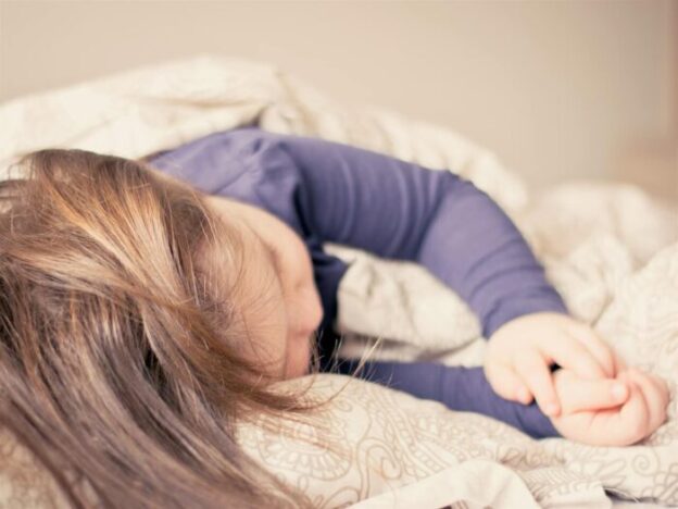 A young girl with dark hair sleeps on a bed