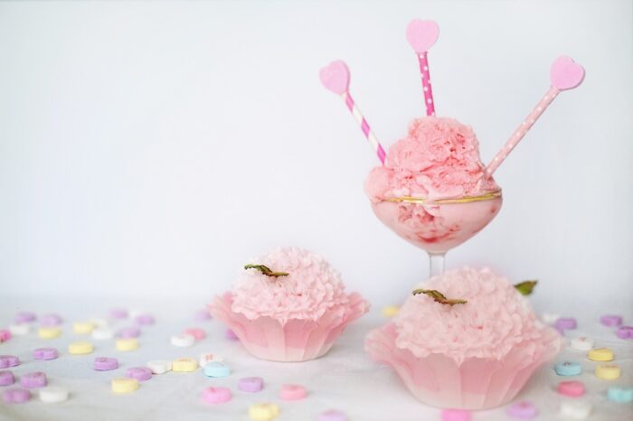 A table covered in heart shape sweets and with 3 pink cakes with fluffy looking pink icing