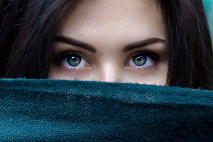 A woman covering the bottom half of her face, showing just her eyes and dark hair