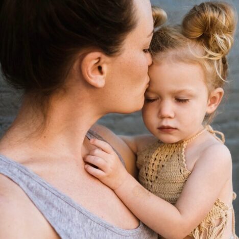 A mother holding her toddler daughter and kissing her head