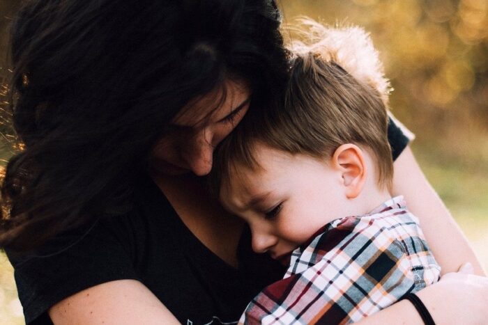 A mother hugging her toddler son, who looks upset