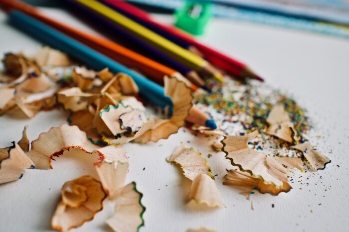 Different coloured pencils lying on a white sheet in a pile of their sharpenings