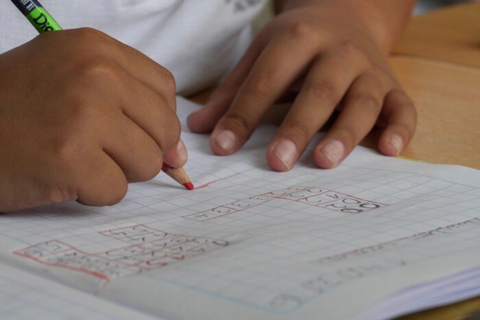 A child's hands writing on a piece of paper. It appears to be some maths work