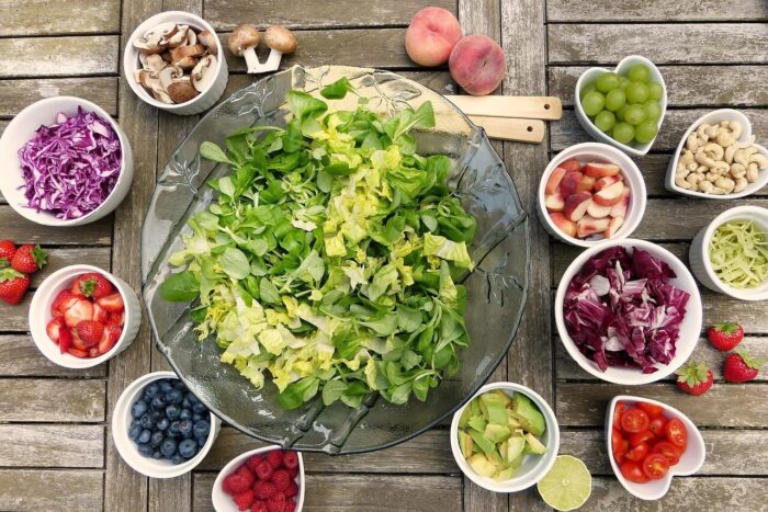 a large bowl pf leaf salad, with multiple dishes surrounding it with various chopped vegetables in them