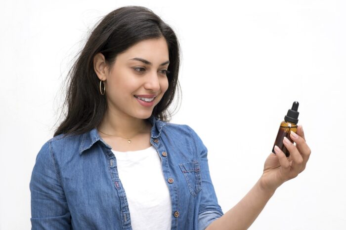A woman with brown skin and long dark hair is looking at a bottle of hair oil